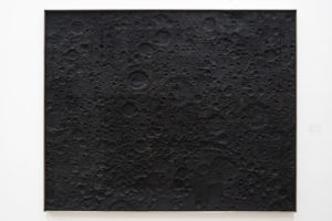 This artwork looks like the surface of the moon. It is completely black and has craters burned into it.