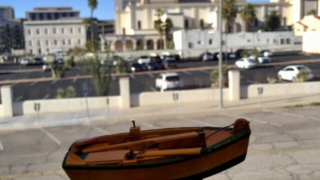 A person displays a small boat against a city backdrop, illustrating the intersection of urban culture and maritime interests.