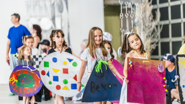 Children in vibrant costumes parade down a hallway, showcasing their colorful attire and joyful expressions.